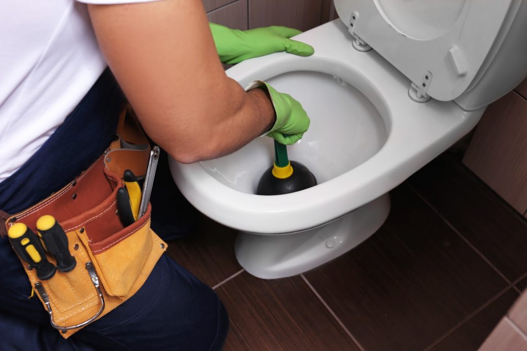 Man plunging toilet with tools